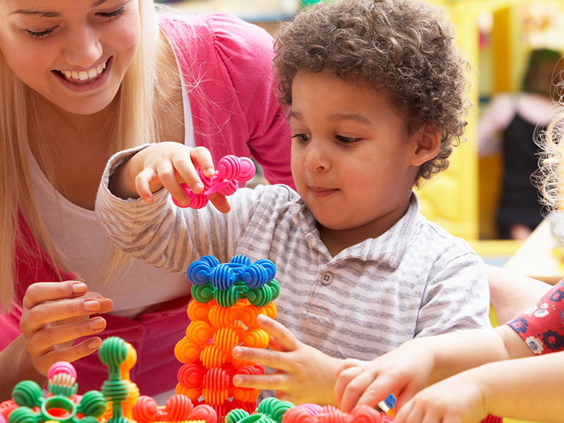 Little boy playing with learning toys with a teacher's aid